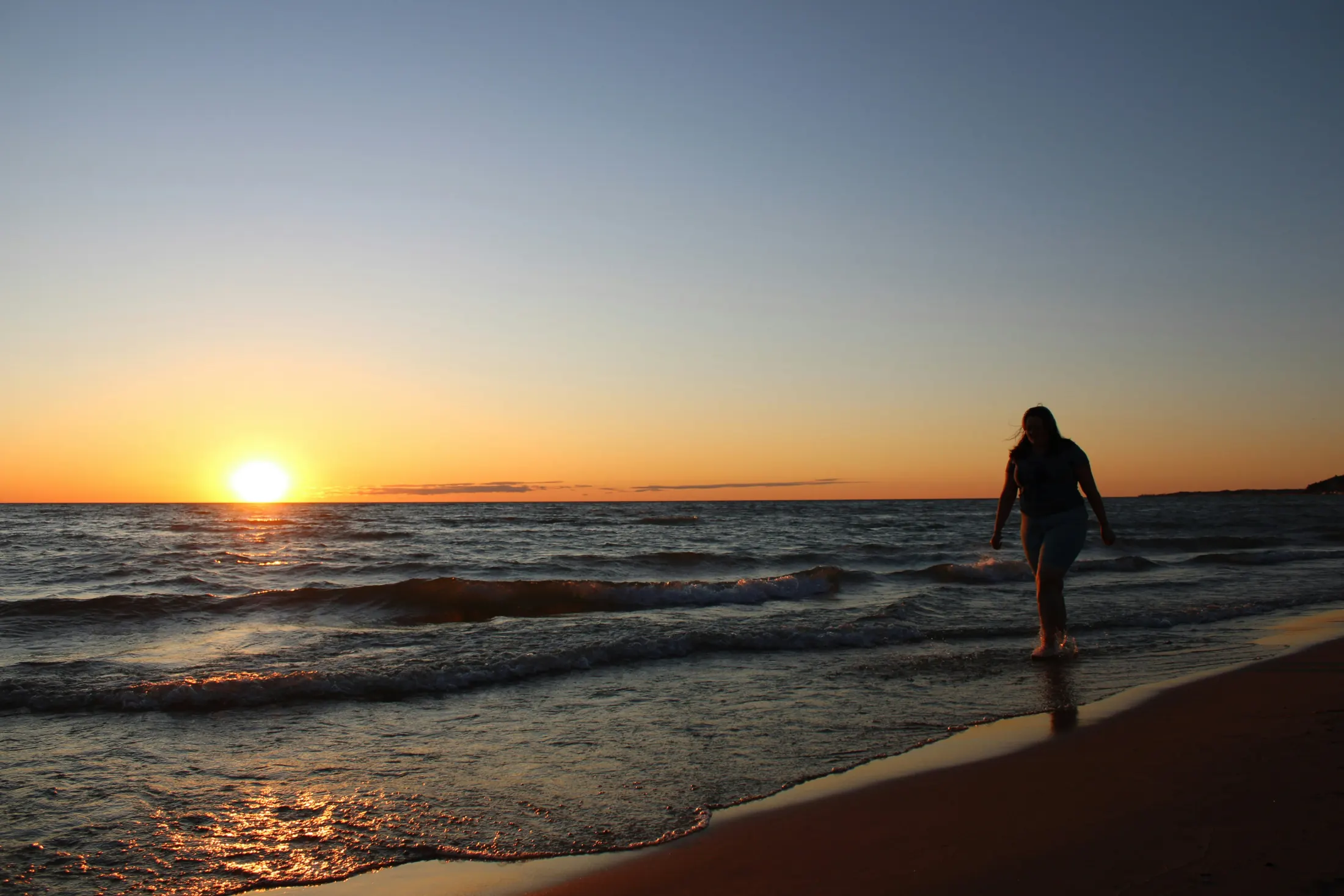 A person walking along a Great Lakes shoreline at sunset