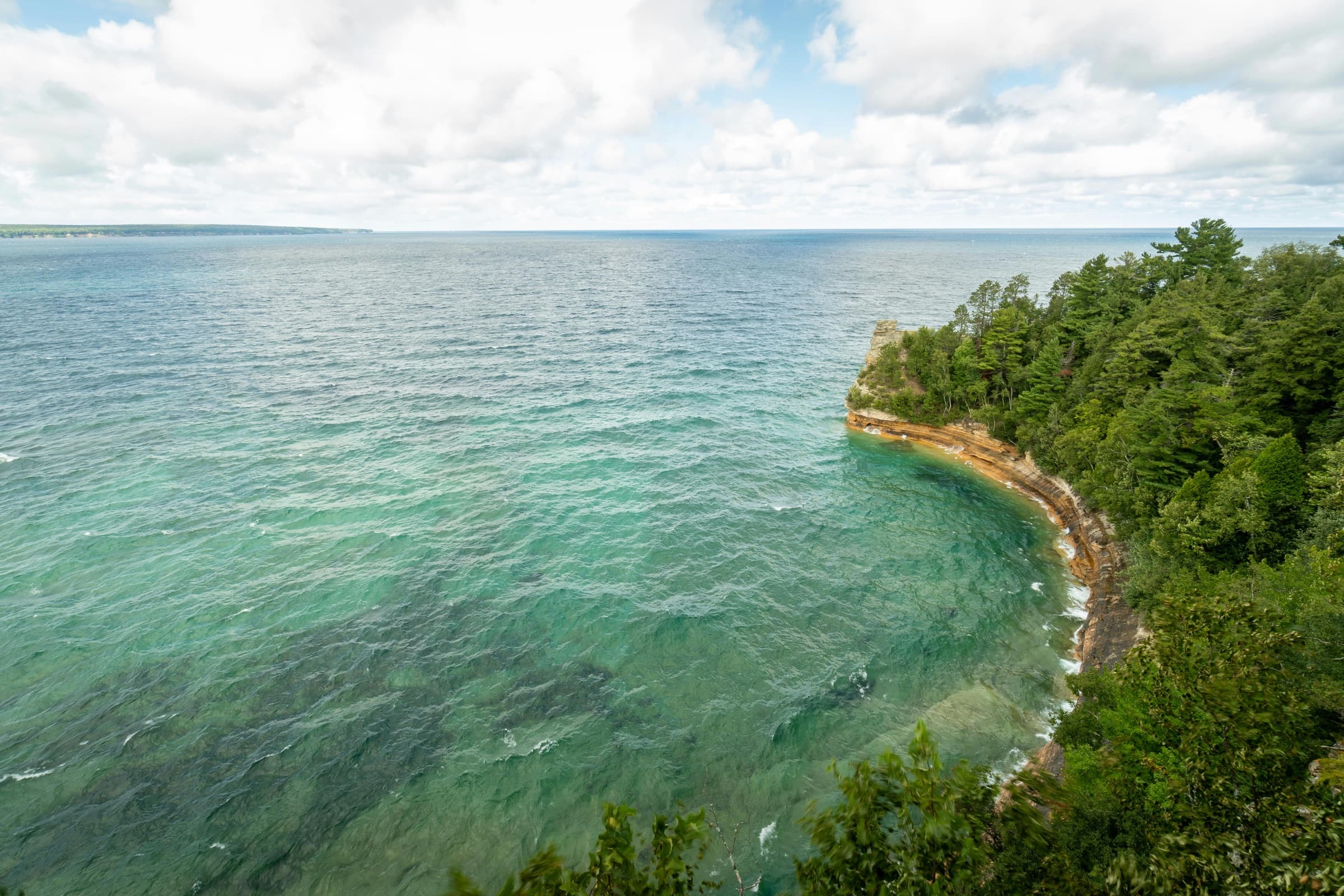 Turquoise Great Lakes water meeting the forested cliffs at Pictured Rocks